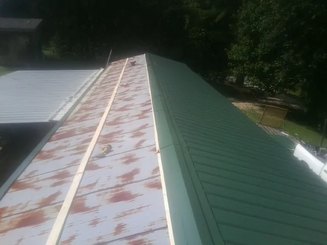 Old rusted panels beside newly installed green metal roofing in Linden