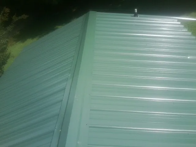 New green metal panels meeting at the ridge of a roof — Flat Roof Repair work by our crew in Linden