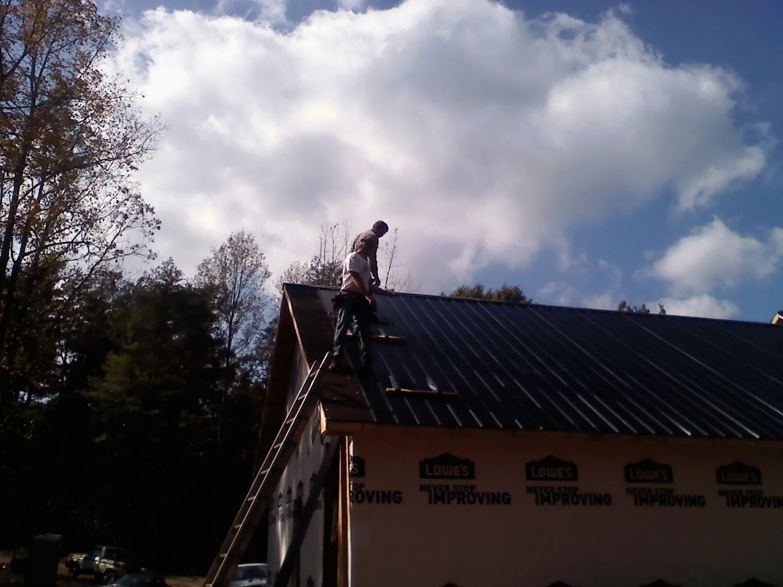 Roofer fastening dark metal panels high against a cloudy sky, from a Roof Inspection job in Linden